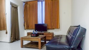 A living room with a leather sofa, a wooden coffee table, a TV on a stand, and curtains on the windows.