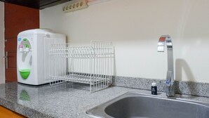 A kitchen with a granite countertop, a stainless steel sink, a white water dispenser, and a metal drying rack.