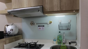 A kitchen with a gas stove, a sink, a dish rack, and a cabinet above the counter. - Comfortable Fully Furnished 2BR Bassura City Apartment (Jakarta)