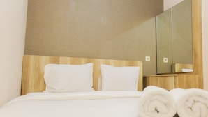 A hotel room with a wooden headboard, a large mirror, and neatly made white pillows and towels. - Comfortable Fully Furnished 2BR Bassura City Apartment (Jakarta)