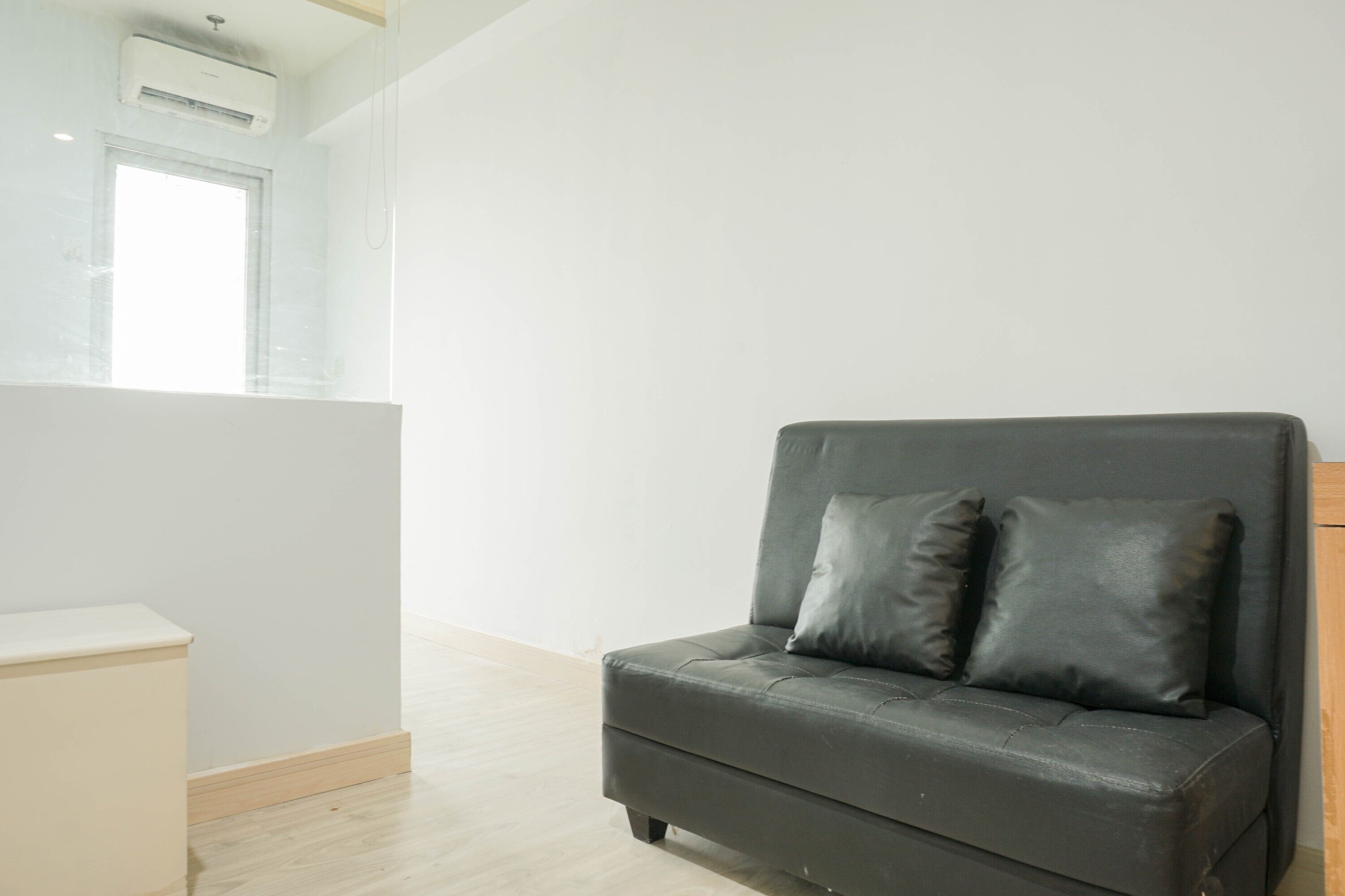 A modern, minimalist room with a grey sofa, two black cushions, a small white table, and a window with blinds.