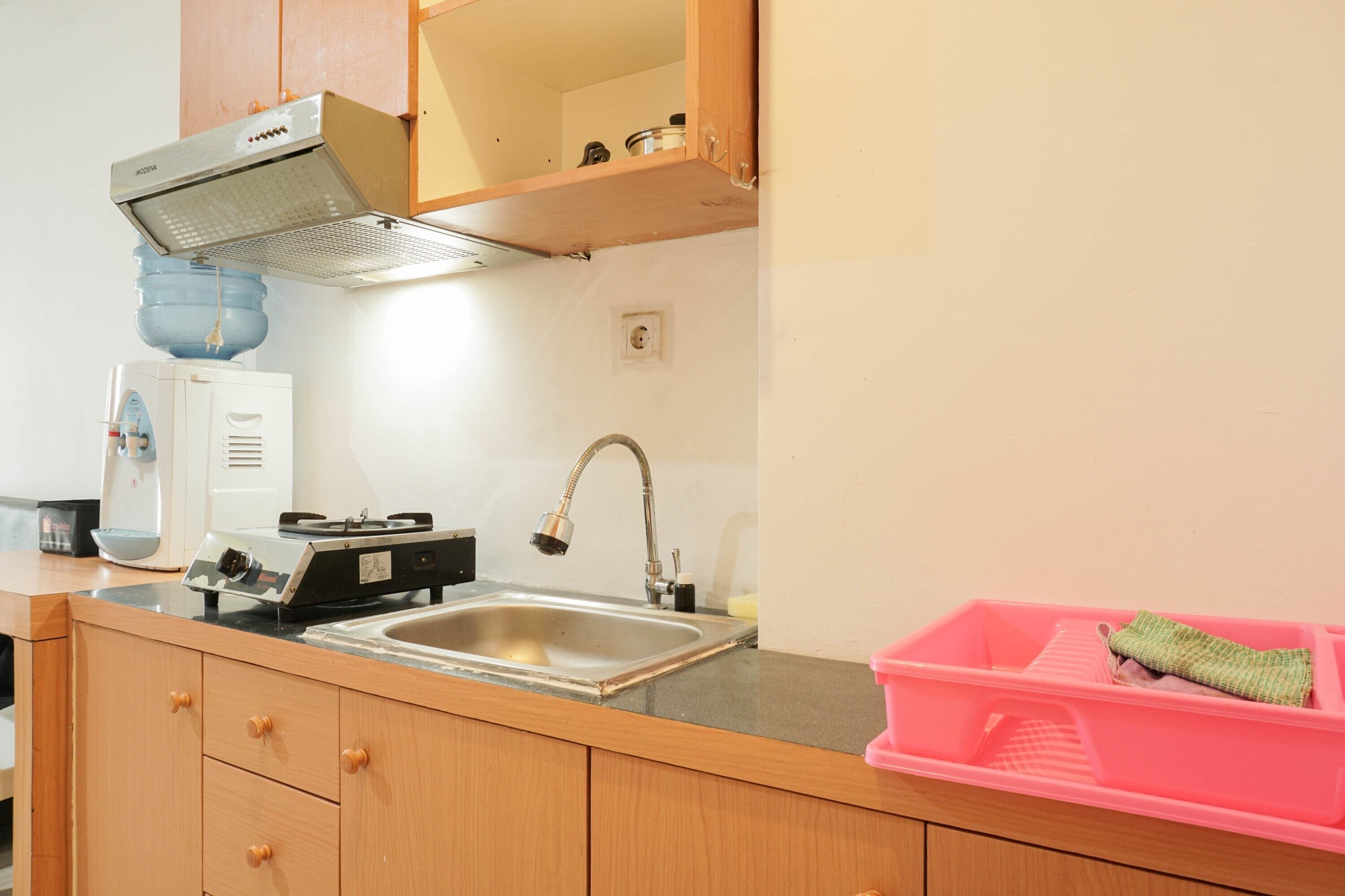 A kitchen with a stainless steel sink, wooden cabinets, a range hood, and a pink dish rack.