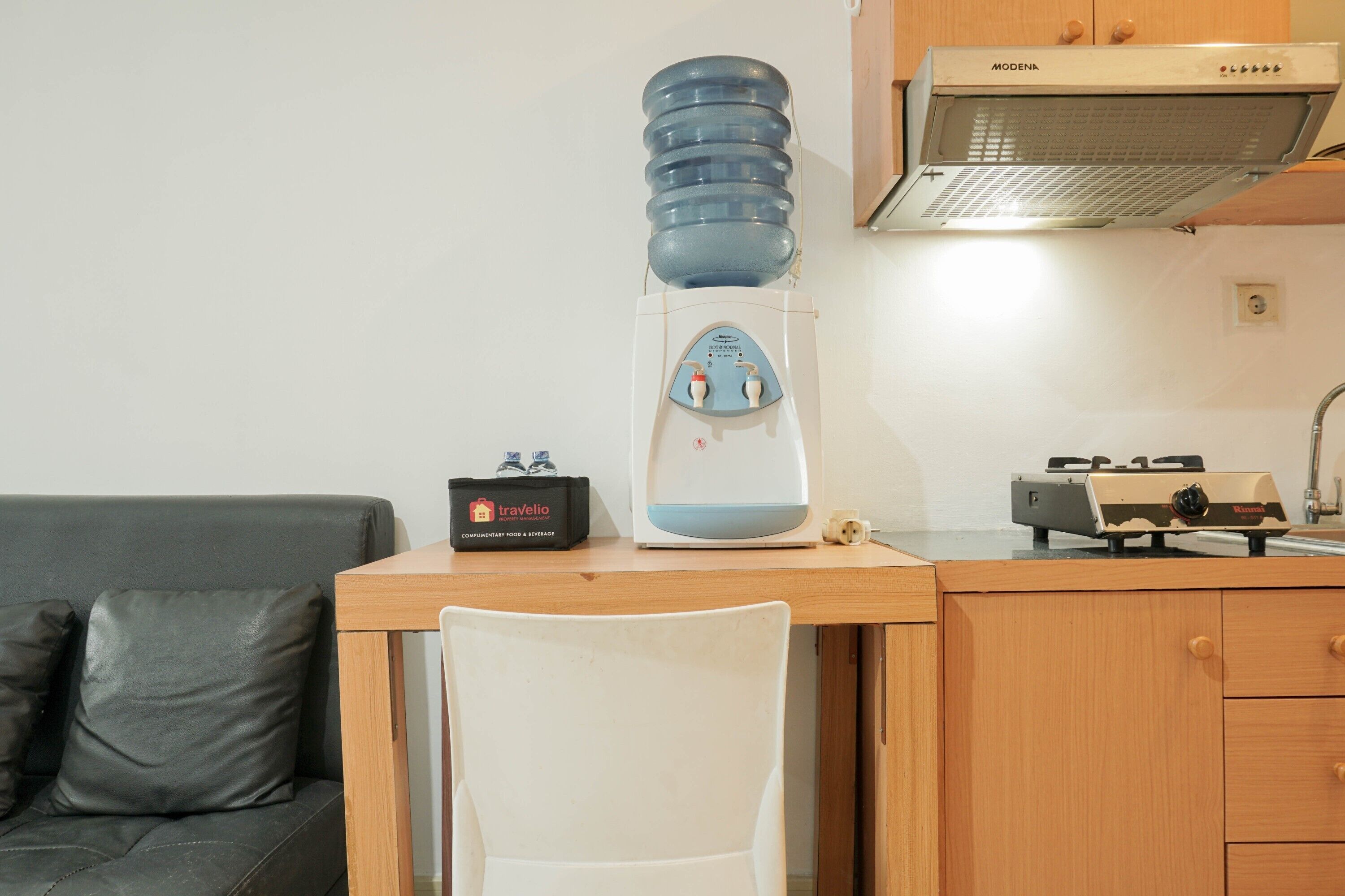 Une petite cuisine équipée d’un distributeur d’eau, d’une cuisinière et d’un sac de voyage posé sur le comptoir.
