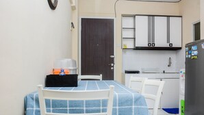 A small kitchen with white cabinets, a refrigerator, and a table with a blue tablecloth. - Comfy 2BR Mutiara Bekasi Apartement (Bekasi)
