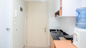 A small kitchenette with a sink, a water dispenser, and a door. - Comfy Studio at The Springlake Summarecon Apartment (Bekasi)