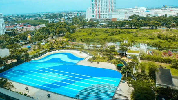 A large swimming pool with a wavy design, surrounded by greenery and a tall building in the background. - Comfy Studio at The Springlake Summarecon Apartment (Bekasi)