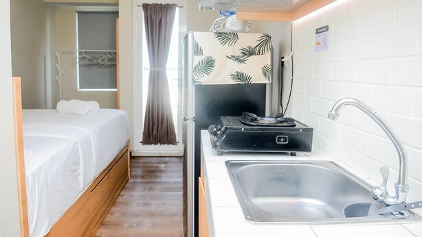 A compact hotel room with a bed, a small kitchenette, a sink, and a window with curtains. - Relaxing Studio at Springlake Summarecon Bekasi Apartment (Bekasi)