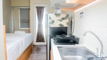 A compact hotel room with a bed, a small kitchenette, a sink, and a window with curtains.