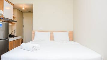 A hotel room with a bed, a small kitchenette, and a door leading to another room.