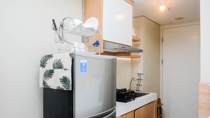 A compact kitchen with a stainless steel refrigerator, a dish rack, a wooden cabinet, and a white countertop. - Relaxing Studio at Springlake Summarecon Bekasi Apartment (Bekasi)