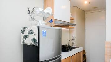 A compact kitchen with a stainless steel refrigerator, a dish rack, a wooden cabinet, and a white countertop.