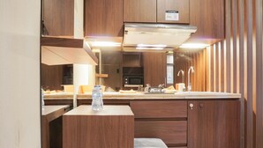 A compact kitchen with wooden cabinetry, a built-in microwave, and a stainless steel range hood. - Comfort Studio Cervino Village Apartment near Casablanca (Jakarta)