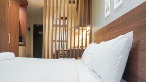 A hotel room with a bed, wooden headboard, and a partition with vertical slats. - Comfort Studio Cervino Village Apartment near Casablanca (Jakarta)