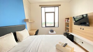 A hotel room with a bed, a desk, a TV, and a window.