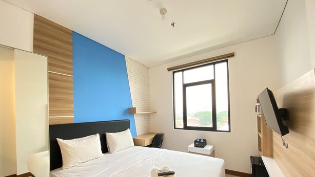 A hotel room with a bed, a desk, a TV, and a window.