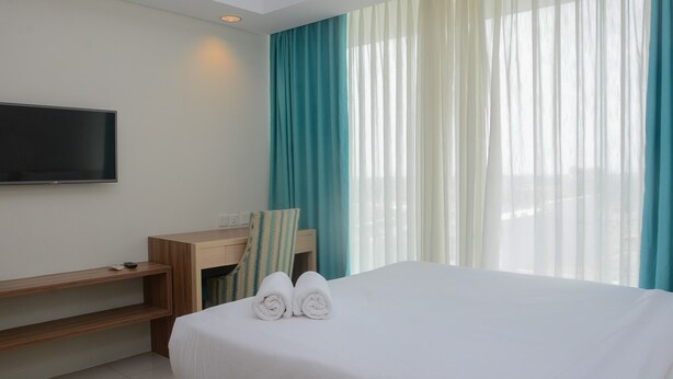 A hotel room with a bed, a TV mounted on the wall, a desk, and a chair.