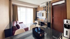 A hotel room with a dining table, a sofa, a TV mounted on the wall, and a minibar. - Luxurious & Cozy 2BR Gateway Pasteur Apartment near Exit Toll (Cimahi)