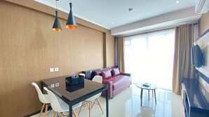 A modern hotel room with a dining area, a red sofa, and a flat-screen TV. - Luxurious & Cozy 2BR Gateway Pasteur Apartment near Exit Toll (Cimahi)