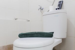 A white toilet with a green bath mat, a showerhead, and a toilet paper holder with a box on top.