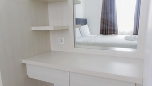 A modern hotel room with a white vanity, a mirror reflecting a bed with white linens, and a window with curtains. - Homey and Cozy 2BR Bassura City Apartment near Mall (Jakarta)