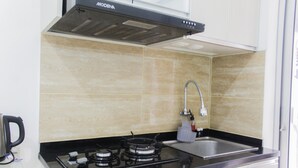 A kitchen with a gas stove, a sink, and a modern range hood. - Homey and Cozy 2BR Bassura City Apartment near Mall (Jakarta)