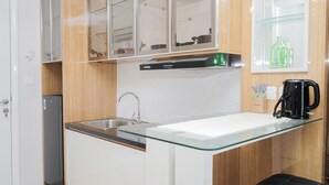 A modern kitchen with a glass countertop, stainless steel sink, and a built-in dishwasher. - Minimalist and Cozy Studio Apartment at Tuscany Residences (South Tangerang)