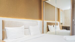 A modern hotel room with a large bed, a bedside table, and a mirror reflecting the room. - Minimalist and Cozy Studio Apartment at Tuscany Residences (South Tangerang)