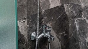 Una ducha con cabezal de ducha de mano y grifo empotrado en una pared de mármol.