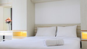 Une chambre d’hôtel avec un grand lit, une table de chevet, un miroir et un vase rempli de fleurs.