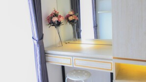 Une coiffeuse blanche avec un miroir, deux vases de fleurs et un tabouret.