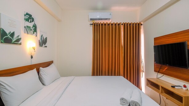 A hotel room with a bed, a TV, an air conditioner, and a curtain. - Comfy Studio at Bogorienze Apartment near The Jungle Waterpark (Bogor)