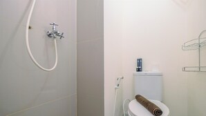 A bathroom with a toilet, a shower, and a towel on the toilet. - Comfy Studio at Bogorienze Apartment near The Jungle Waterpark (Bogor)