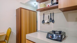 A compact kitchen with a gas stove, wooden cabinets, and a yellow chair. - Comfy Studio at Bogorienze Apartment near The Jungle Waterpark (Bogor)