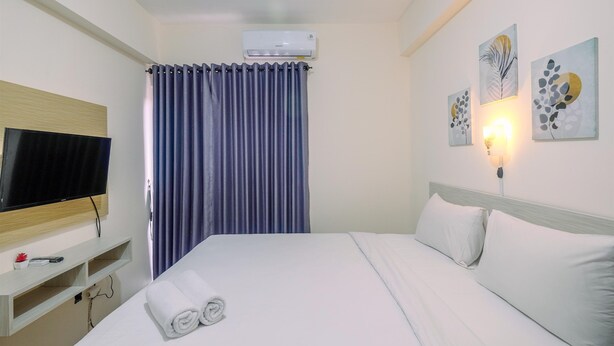 A hotel room with a bed, a flat-screen TV, an air conditioner, a wall-mounted light, and artwork.