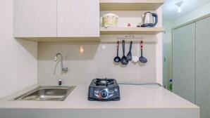 A compact kitchen with a gas stove, a sink, and a kettle on a shelf.