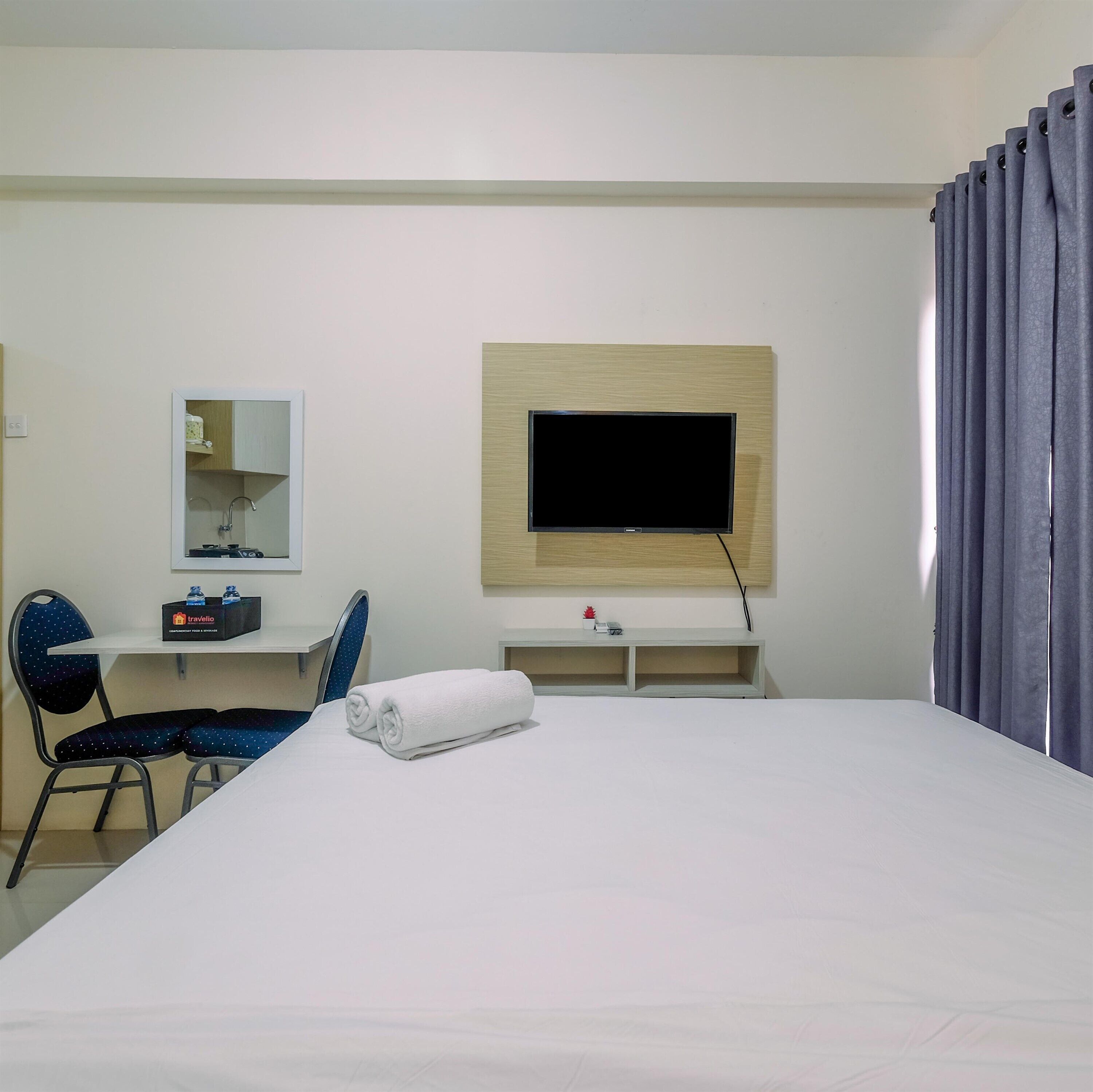 A hotel room with a bed, a desk, a chair, a television mounted on the wall, and a window with curtains.