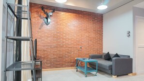 A modern living room with a brick wall, a grey sofa, a teal coffee table, and a metal shelf unit. - Luxurious 1BR Apartment at Belmont Residence (Jakarta)