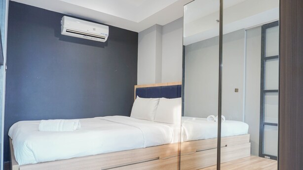 A modern bedroom with a bed, a mirror, and an air conditioning unit. - Luxurious 1BR Apartment at Belmont Residence (Jakarta)