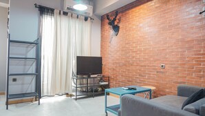 A living room with a brick wall, a mounted deer head, a television on a stand, a sofa, and a small table. - Luxurious 1BR Apartment at Belmont Residence (Jakarta)