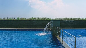 A swimming pool with a water feature, surrounded by a low stone wall and greenery. - Luxurious 1BR Apartment at Belmont Residence (Jakarta)