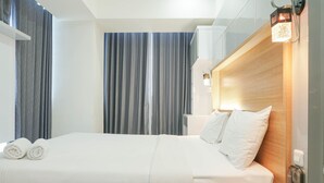 Een moderne hotelkamer met een netjes opgemaakt bed, een houten hoofdeinde en een groot raam met gordijnen.