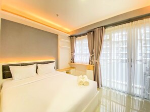 Una habitación de hotel moderna con una cama grande, una mesita de noche y un ventanal con cortinas.
