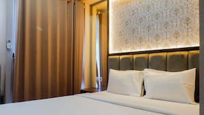 Une chambre d’hôtel avec un lit bien fait, une tête de lit recouverte d’un papier peint à motifs et un rideau sur le côté gauche.