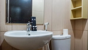Une salle de bain avec un lavabo blanc, un miroir, des toilettes et une étagère contenant des articles de toilette.