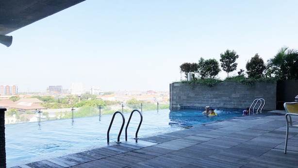 Une piscine à débordement offrant une vue sur la ville, un mur en béton agrémenté de verdure et une terrasse carrelée.