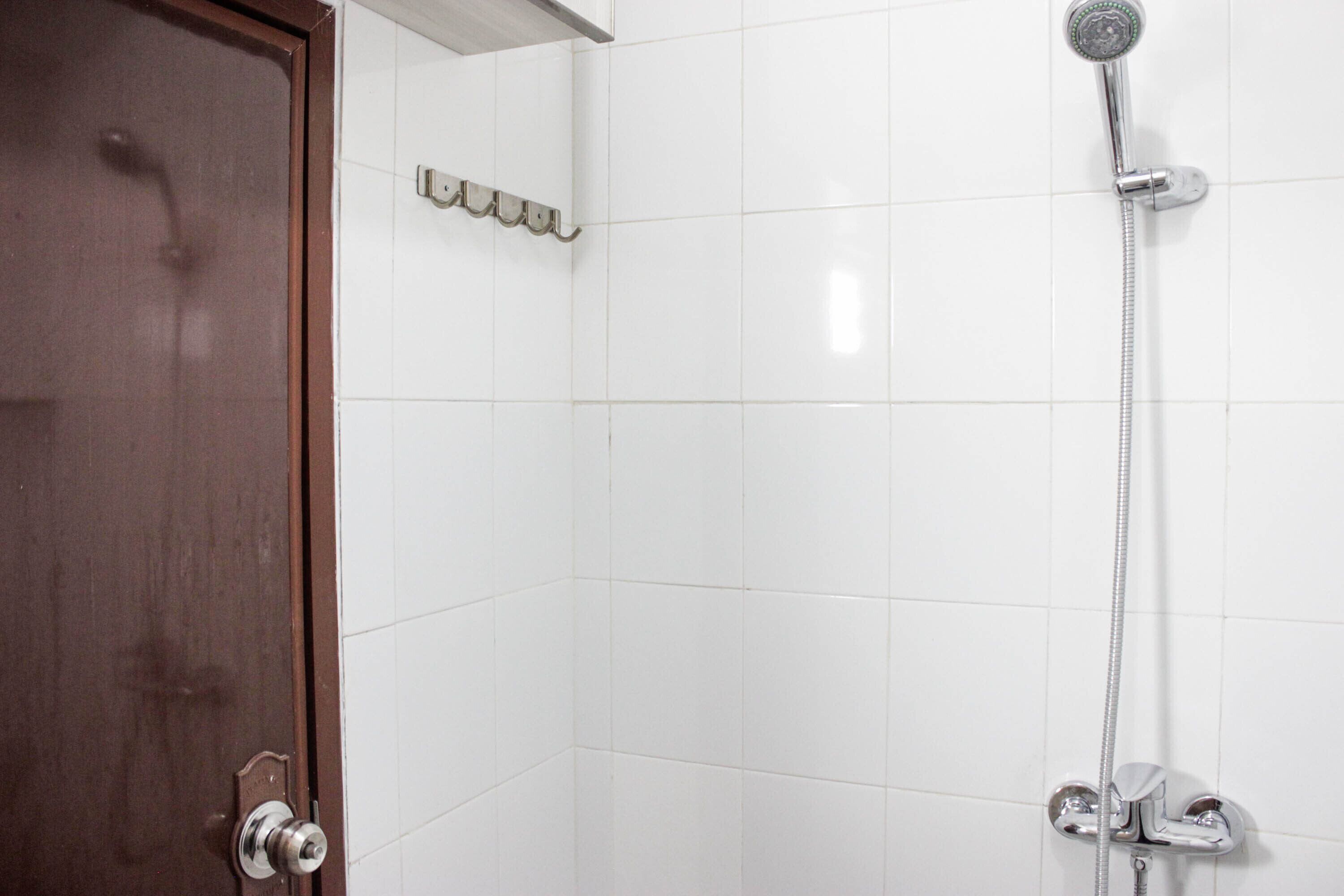 Bagno con pareti piastrellate di bianco, doccia con soffione a mano e porta in legno.