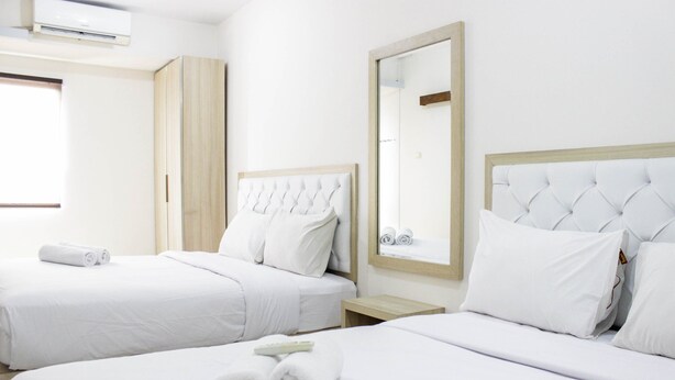 Quarto de hotel com duas camas, roupa de cama branca, guarda-roupa de madeira, espelho e janela.