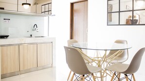 Cozinha moderna com mesa de jantar de vidro e quatro cadeiras, armários de madeira e luminária pendente.