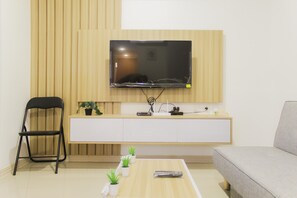 Ein modernes Wohnzimmer mit einem an der Wand montierten Flachbildfernseher, einem schwarzen Klappstuhl, einem grauen Sofa, einer weißen Kommode und einem kleinen Couchtisch mit Topfpflanzen.
