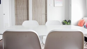 Une salle de conférence avec une table et des chaises blanches, deux portes en bois, une horloge et une œuvre d’art encadrée au mur.
